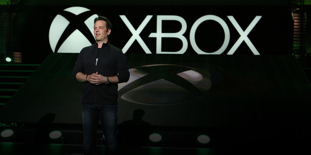 O diretor da Xbox Phil Spencer em cima de um palco em frente ao logótipo da Xbox