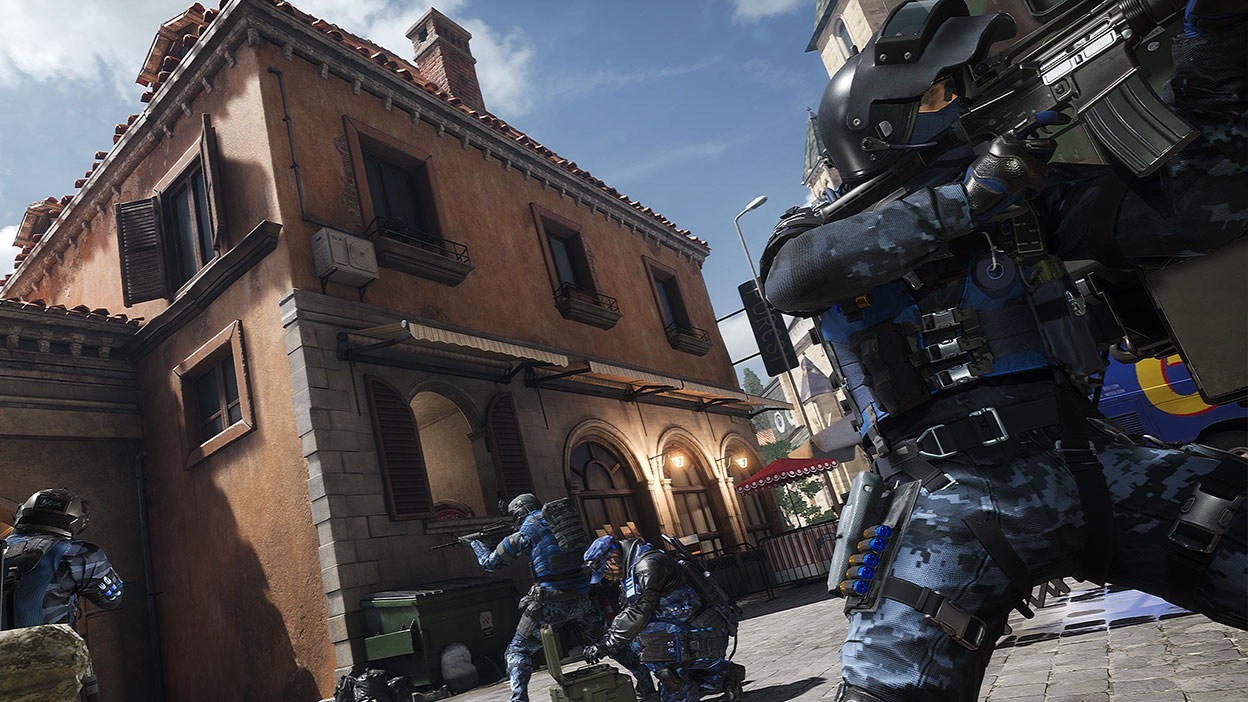 Three mercenaries aim their guns and watch over a teammate setting up equipment in a side alleyway.
