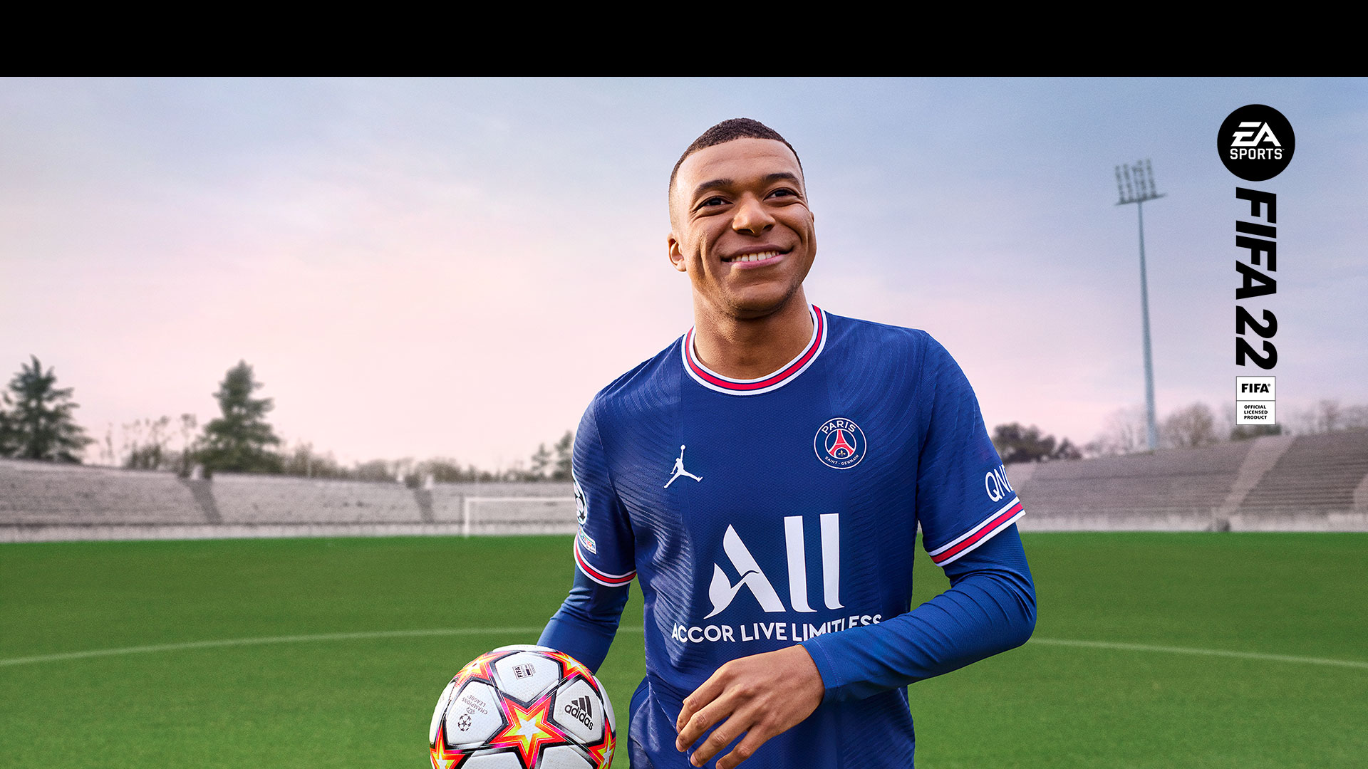 EA Sports、FIFA 22 公式ライセンス製品、人影のないスタジアムで笑顔のプレイヤーがボールを持っている。