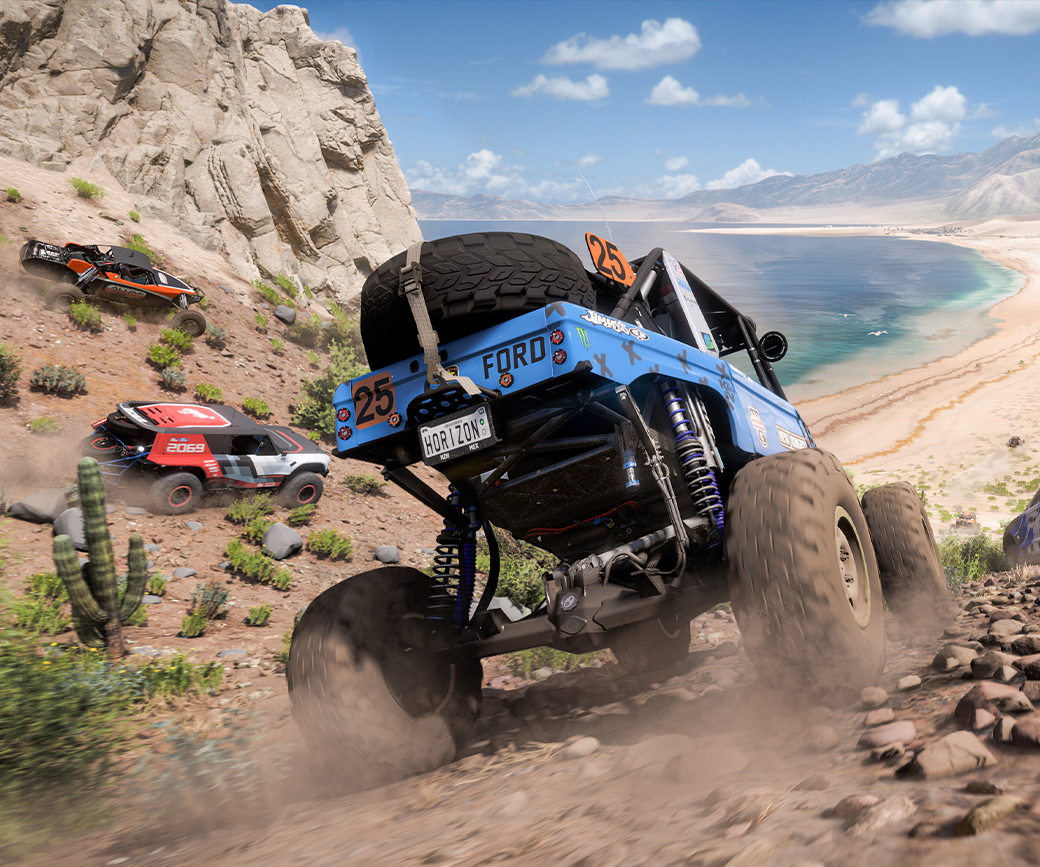 W grze Forza Horizon 5 cztery samochody przyspieszają, jadąc po skalistym terenie w kierunku plaży.