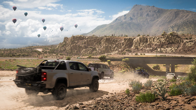 Forza Horizon 5. A truck races down a dirt road with a sky full of hot air balloons in the background.