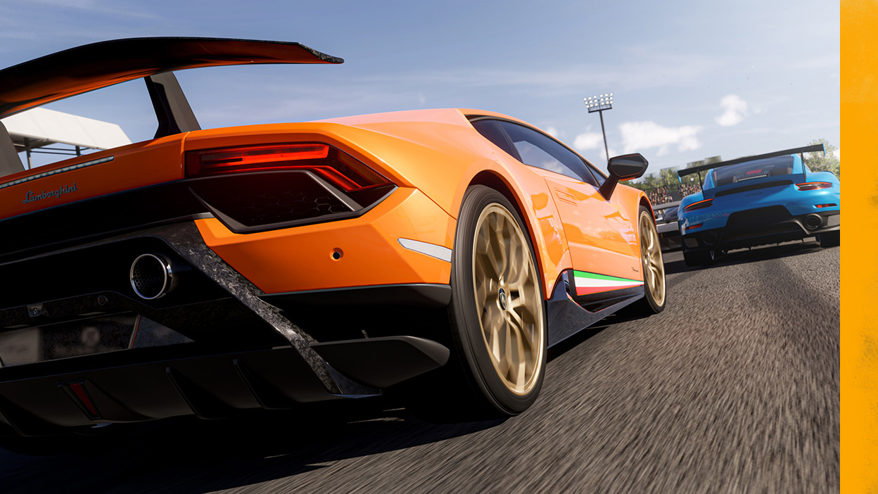 A Lamborghini races down the track behind a blue car.