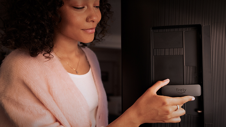 Una mujer conecta su dispositivo Amazon Fire TV a la parte trasera de un televisor