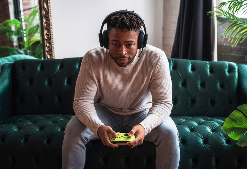 A person wearing a headset playing Xbox games on the sofa.