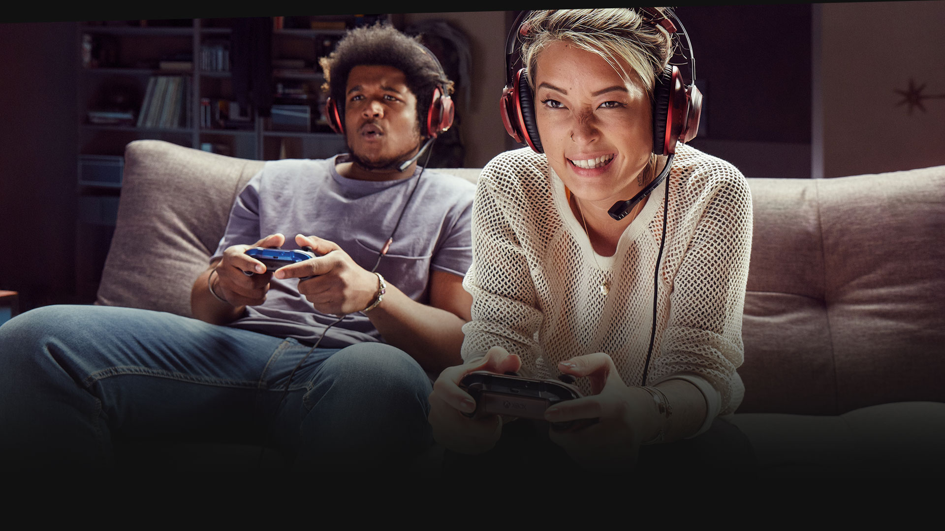 Dvaja ľudia s náhlavnou súpravou hrajúci Xbox One na gauči