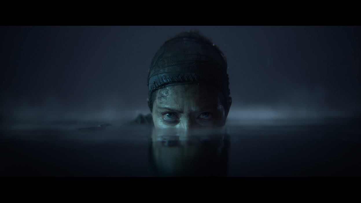 Senua peeks up from under the water in a dark cave.