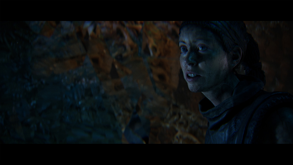 Senua skærer ansigt i en mørk grotte.