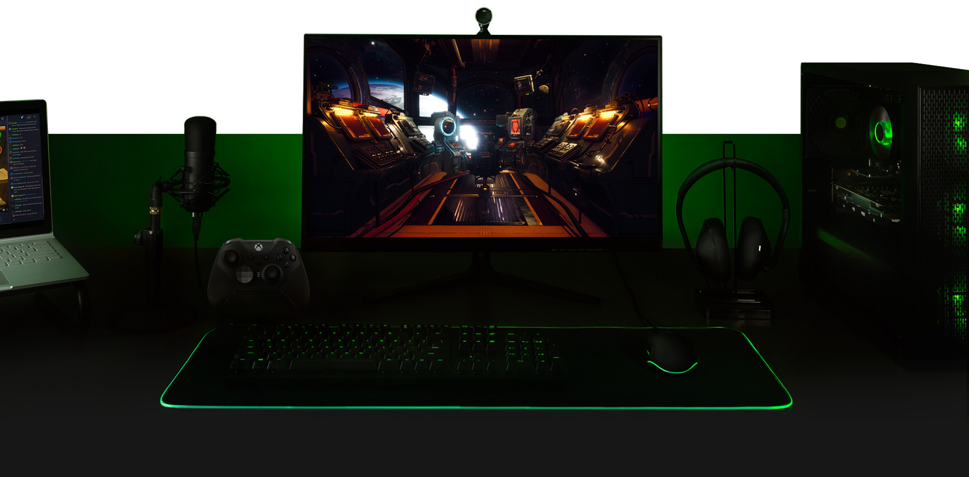 Stolní počítač s počítačem, monitor s obrazovkou ze hry The Outer Worlds, klávesnice, ovladač Xbox One, mikrofon a přenosný počítač připravené společně.