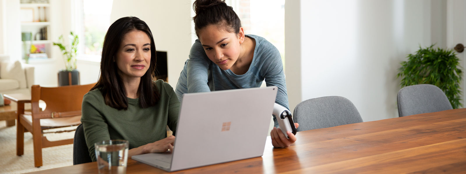 Une mère utilisant son ordinateur portable à côté de sa fille tenant une manette Xbox