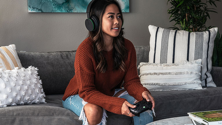 A woman wearing a headset and playing a game with an Xbox controller