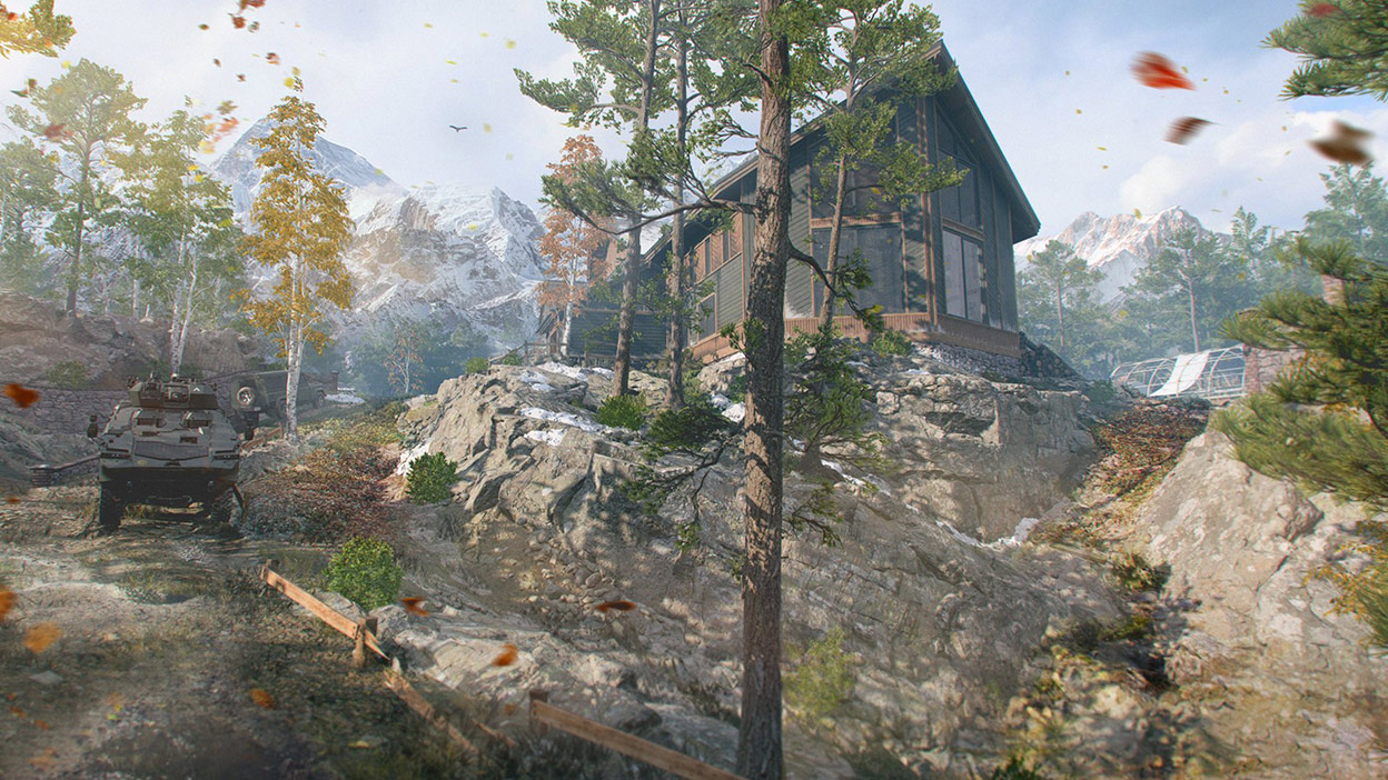 A tank drives down a mountain road surrounded by trees in fall colors and a large cabin.