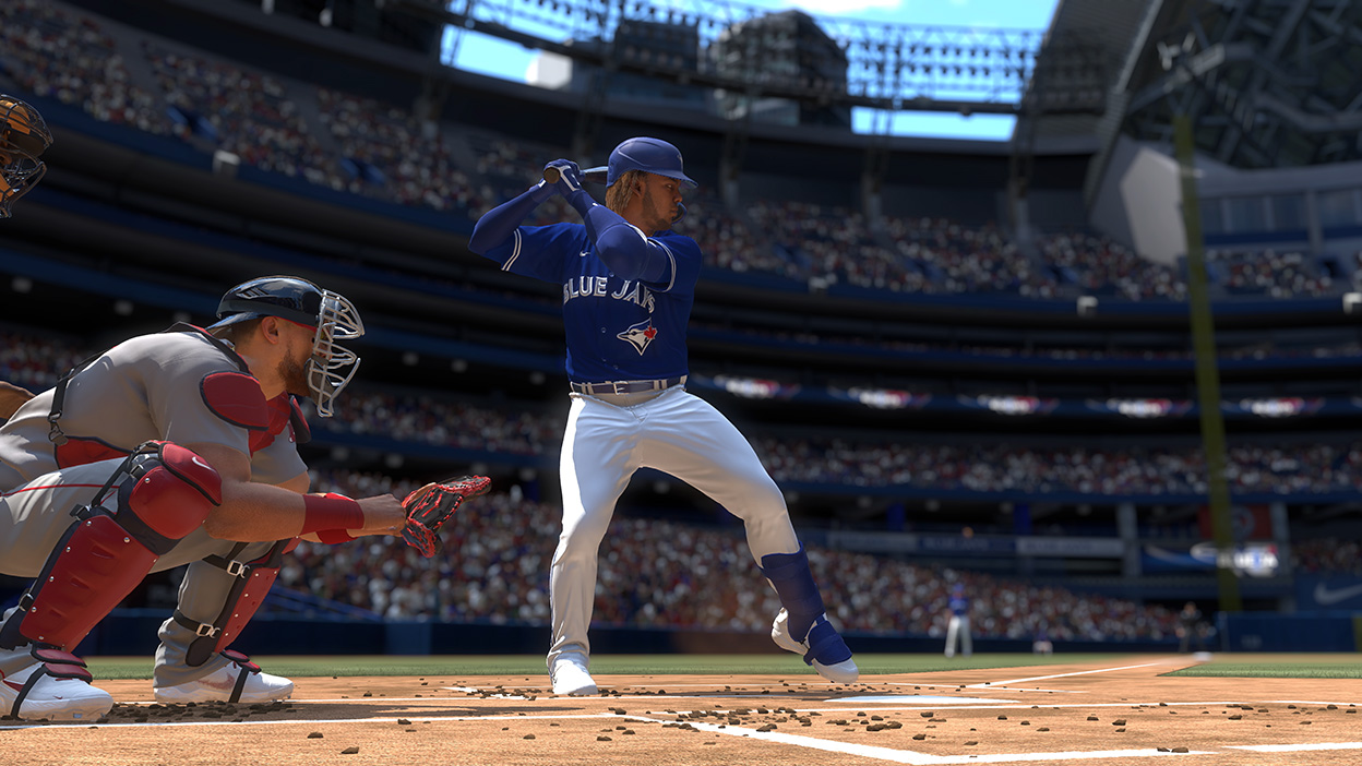 A player for the Blue Jays standing on home base lifts his left foot to swing his bat as the catcher squats down low.