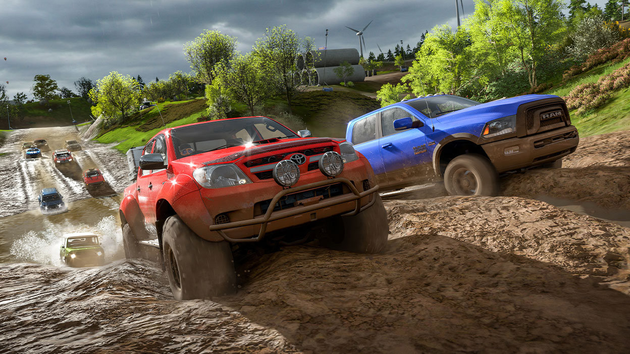 A Toyota pickup and a Dodge Ram cut through a muddy countryside track, in the lead