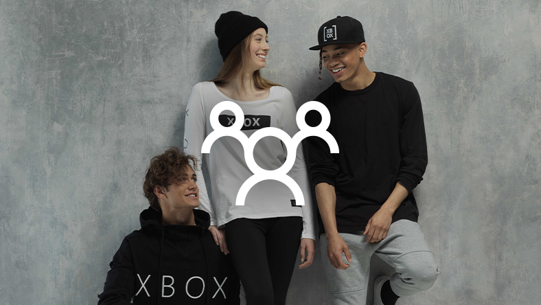 Grupa uśmiechniętych ludzi ubranych w oficjalną odzież Xbox, na którą nałożono zarys trzech postaci ludzkich
