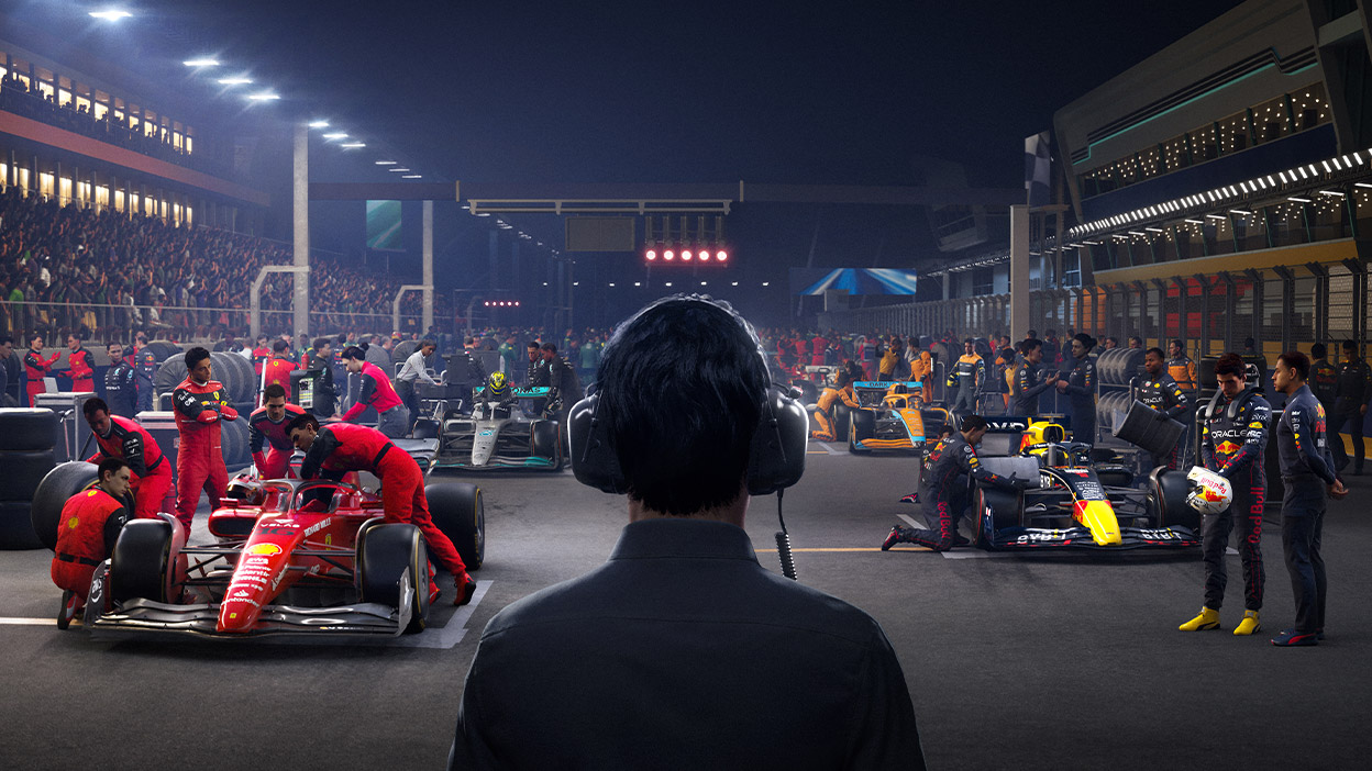 A Formula One manager monitors the progress of pit crews preparing for a nighttime race.