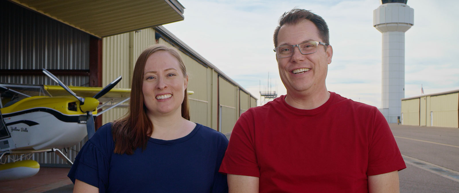 Pilot Hancock and his wife smile outside an airport hanger. 