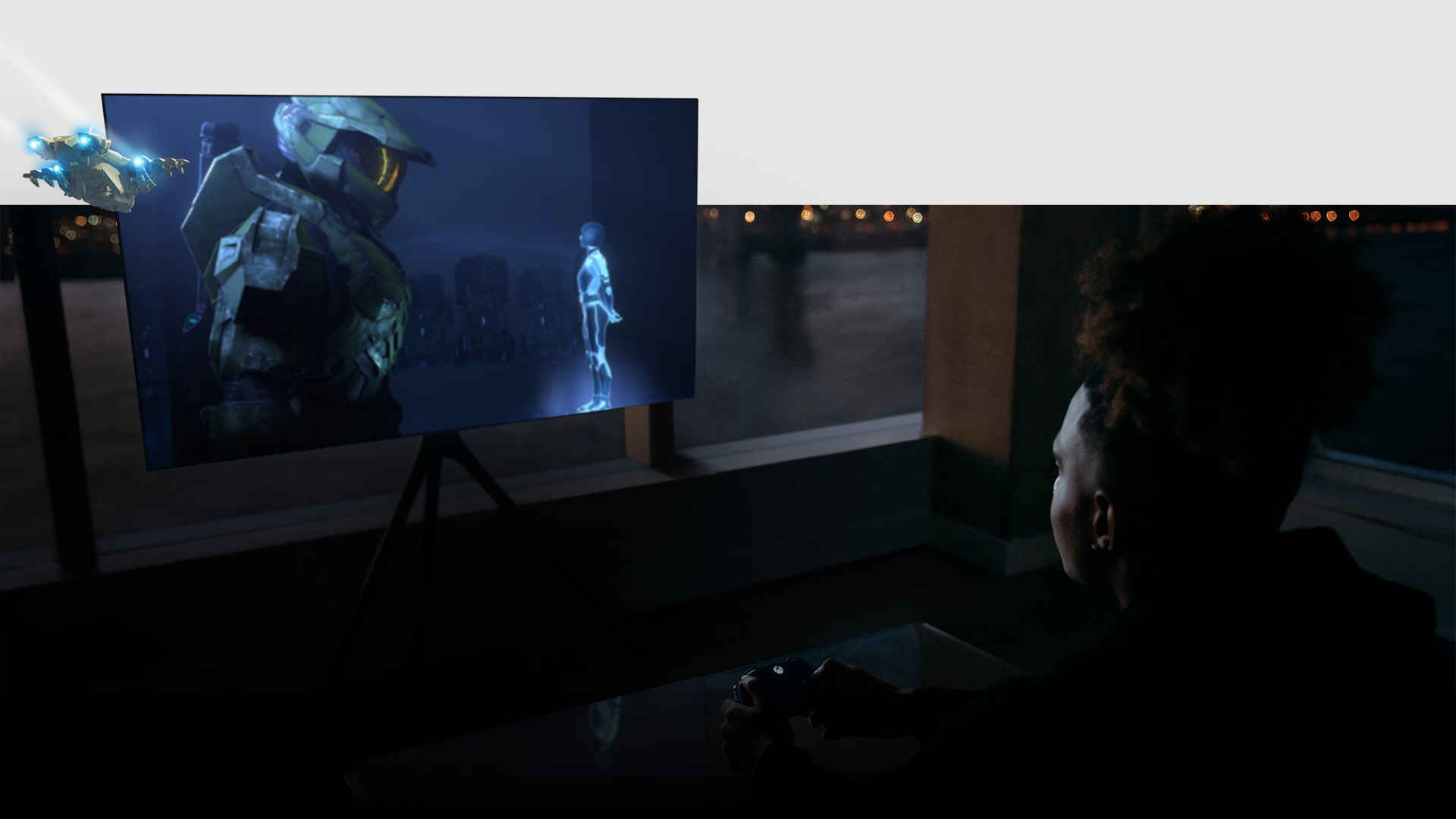 Hráč v obývacím pokoji drží ovladač a na televizoru Samsung běží hra Halo Infinite