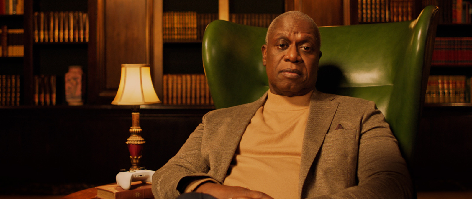 Andre Braugher reclines in a green chair, an Xbox controller on the end table.
