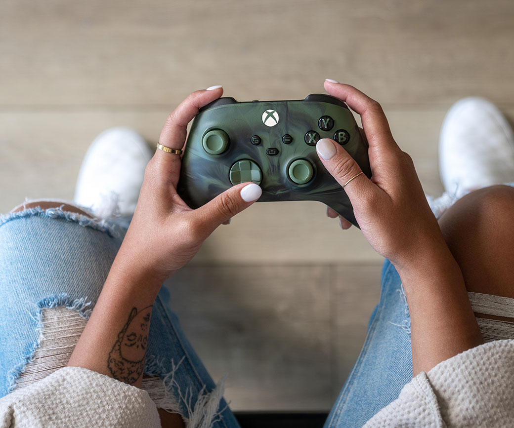 Hráč vo svojej obývačke drží bezdrôtový ovládač Xbox – Nocturnal Vapor Special Edition.