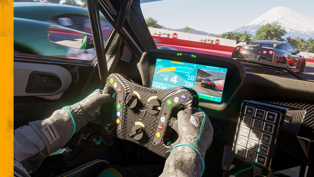 A racer looks down at the steering wheel and a digital dashboard.