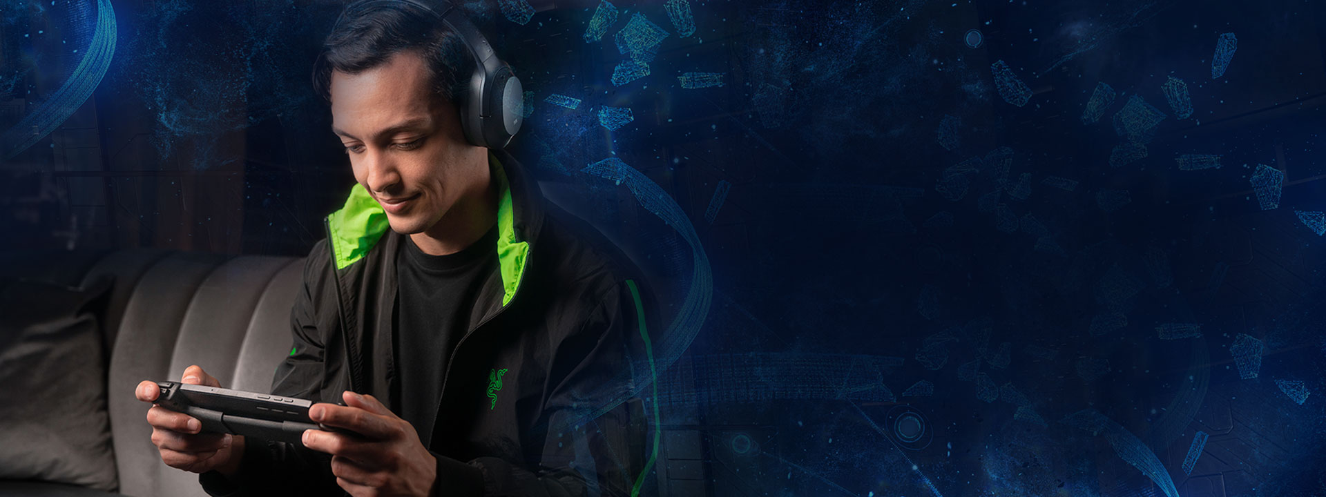 Man on a couch wearing headphones and playing the Razer Edge.