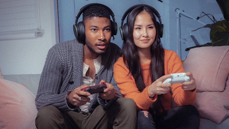 Два человека держат геймпады Xbox и вместе играют в многопользовательские игры.