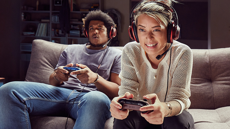 Two people holding Xbox controllers play multiplayer games together
