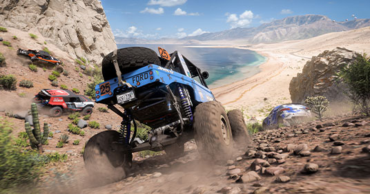 Forza Horizon 5. Several off-road cars drive down a hill towards the beach.