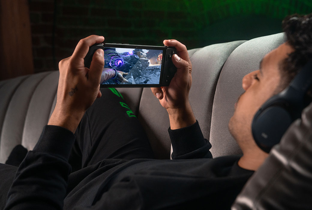 Looking over the shoulder of a person laying on a couch playing the Razer Edge.