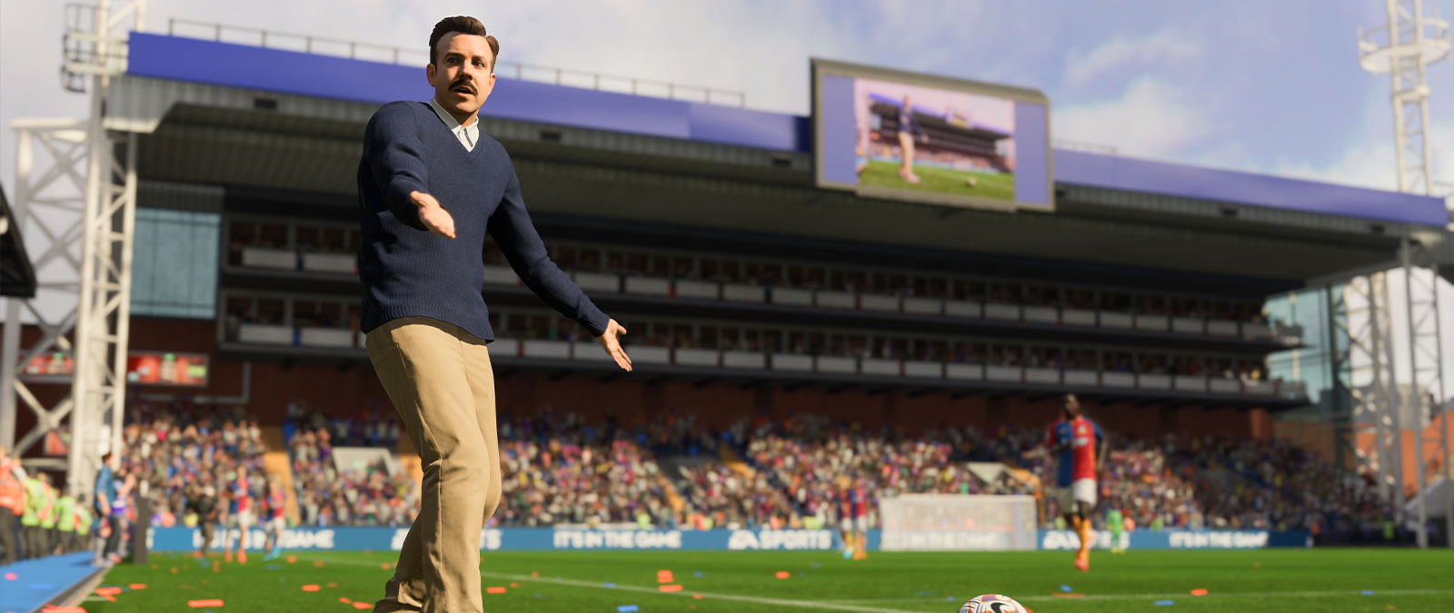 Ted Lasso holds his arms out in confusion on the soccer field while approaching the ball.