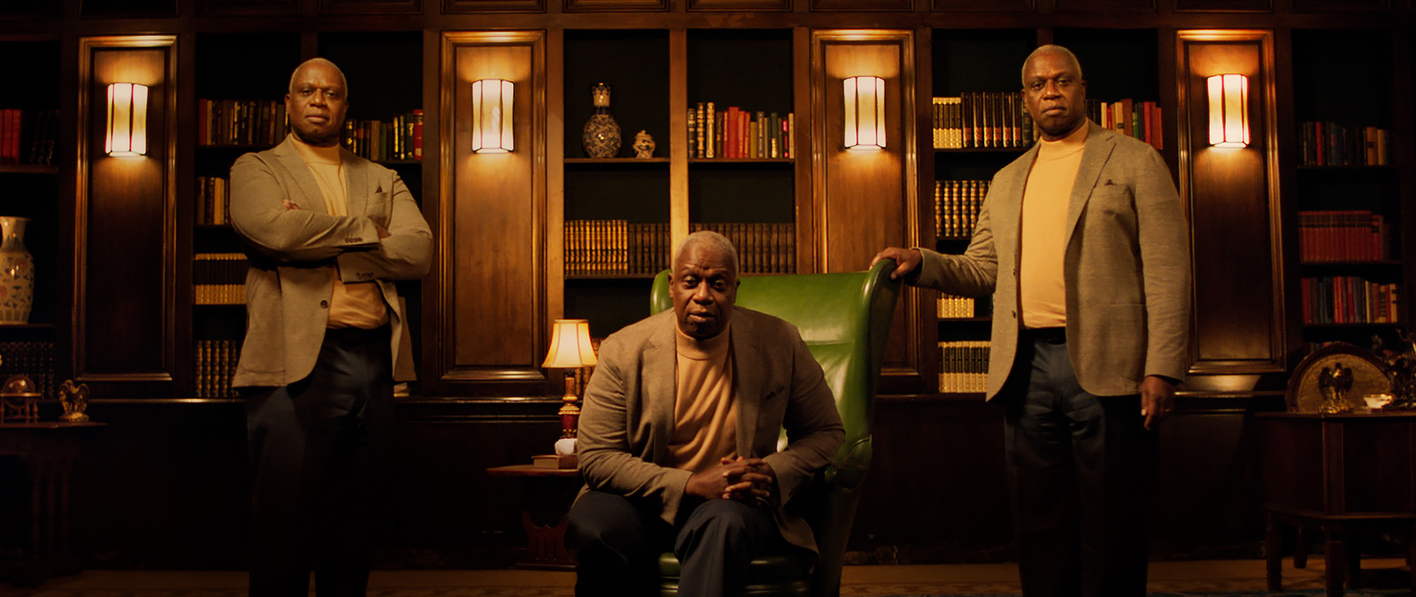 Andre Braugher sits in a green chair, with two more Andres standing to his left and right.